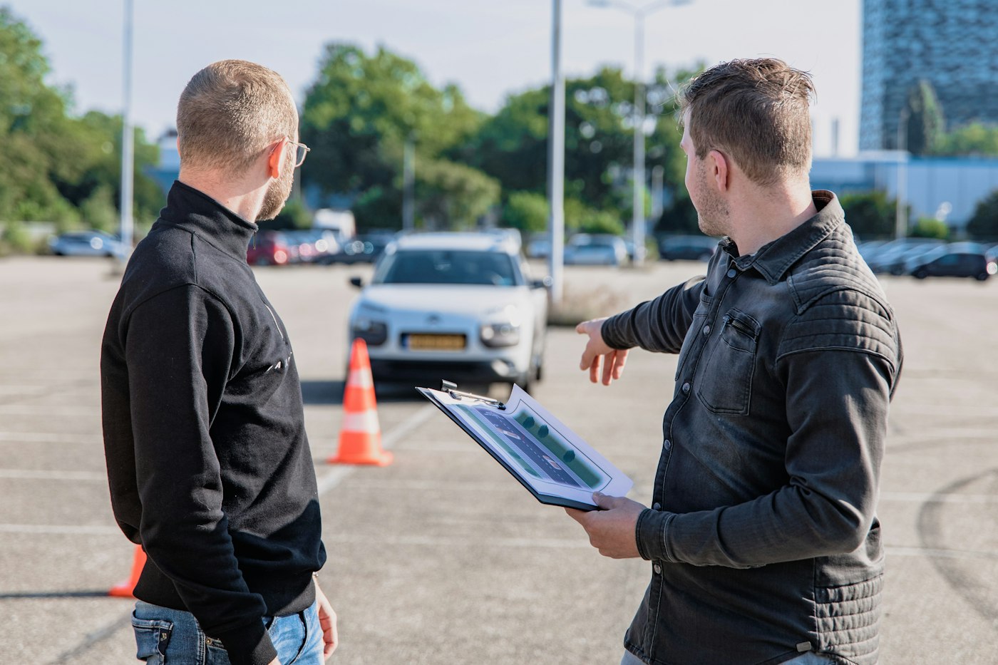 Moniteur avec un porte-documents devant une voiture, sur une piste balisée de plots